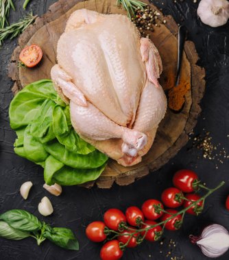 Whole raw chicken on a wooden board with spices for cooking, top view
