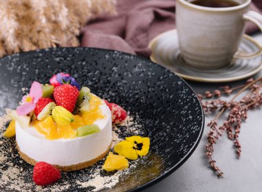 Round cheesecake with fruit decoration and cup of coffee