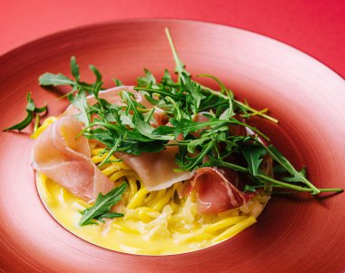 Prosciutto ve kırmızı tabakta roka ile spagetti.
