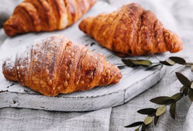 Close up three freshly baked croissants with sugar powder on a wooden desk