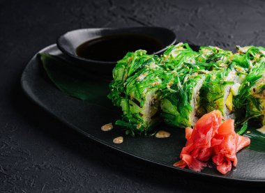 Suşi rulolarını siyah tabakta yosunların içine koy.