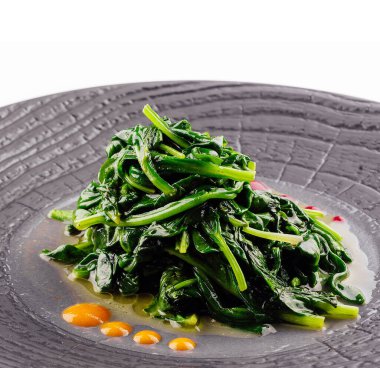 Fried spinach on black plate isolated