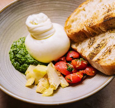 Taze sebze salatası, beyaz yumuşak burrata peyniri ve yeşil pesto yakın plan.