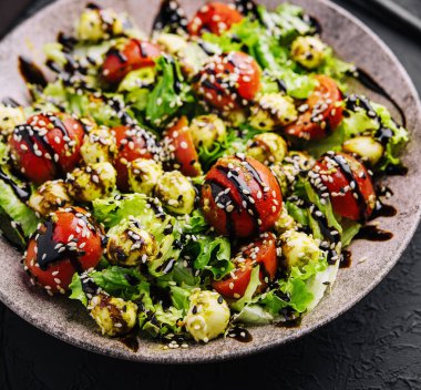 Green salad made with tomatoes, cheese mozzarella balls and sesame on plate