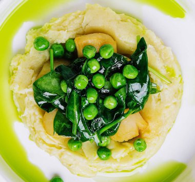 Mashed potato with butter, green peas, basil in a white bowl