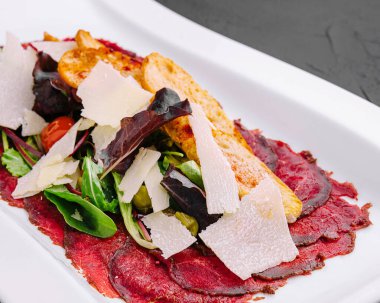 Salatalı biftek carpaccio ve beyaz tabakta parmesan.