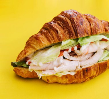 Sarı arka planda kruvasan sandviçi.