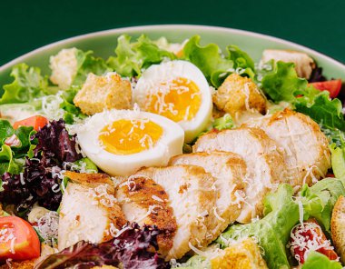Caesar salad with chicken breast on green background