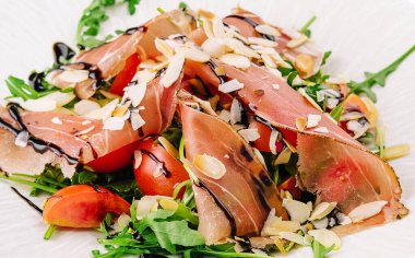 Salad with prosciutto, tomato, arugula leaves on plate