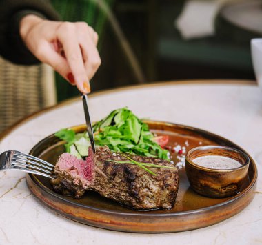 Masadaki bir restoranda, biftek dilimlenmiş bir biftekte kadın eli.