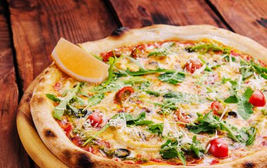 Pizza with arugula, cheese, yoghurt and cherry tomatoes closeup