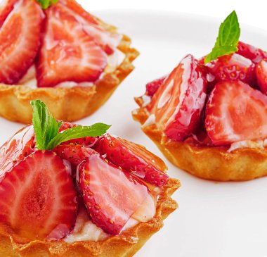 Tartlets with custard, strawberries and mint served on white plate