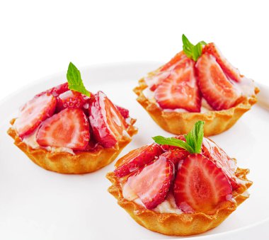 Tartlets with custard, strawberries and mint served on white plate