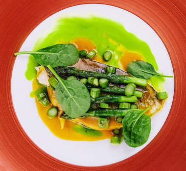 Fish dish - fried cod fillet with asparagus and basil served on red plate