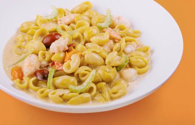 Sarı arka planda karidesli İtalyan yemeği.