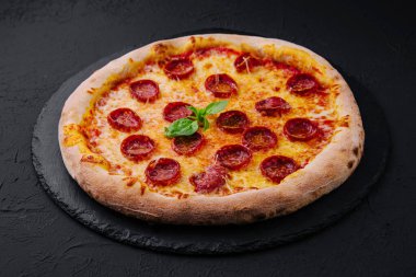 Siyah taş tabakta Basil ve Parmesan peynirli Pepperoni Pizza.