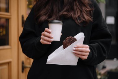 Elinde bir kupa kahve ve elinde yulaflı kurabiye tutan bir kadın.