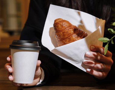 Kahve dükkanında elinde bir kupa kahve ve kruvasan tutan bir kadın.