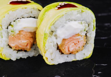 Rolls wrapped in avocado with fried salmon inside