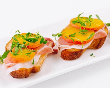 Jambonlu bruschetta ve beyaz tabakta armut.