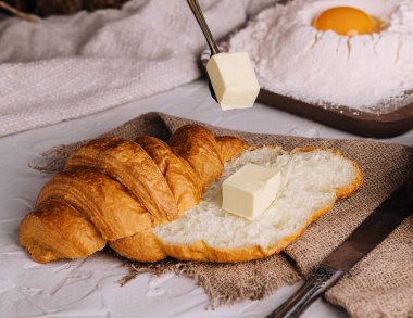 Eller taze kruvasan kesiyor ve tereyağı yayıyor.