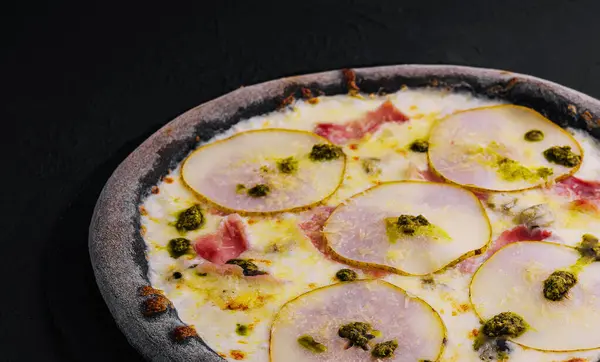 black pizza with pear, cheese and ham