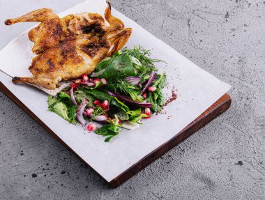 Roasted grilled quail on wooden cutting board with garnish green salad