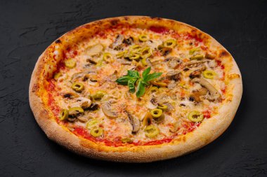 Mantarlı, zeytinli, peynirli ve fesleğenli lezzetli pizza, koyu bir yüzeyde sunulur.