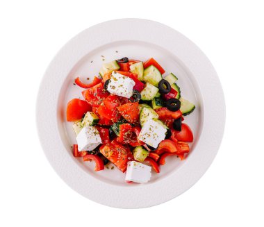 Beyaz bir tabakta servis edilen renkli bir Yunan salatasının beyaz arka planda izole edilmiş hali.