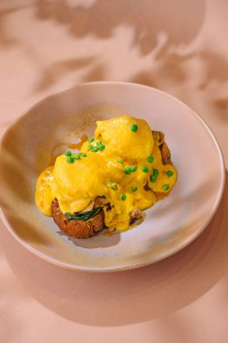 Lezzetli yumurtalar kepekli tost ile servis edilir, kremalı hollandaise sosuyla kaplanır ve soğanla süslenir.