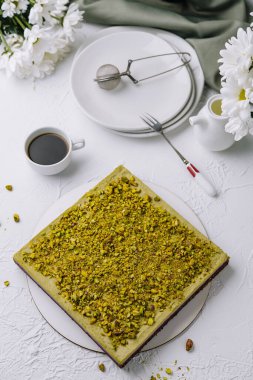 Kahve fincanı, çiçek dekoru ve klasik tatlı çatalıyla beyaz bir tabakta servis edilen enfes şam fıstıklı kek.