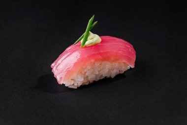 Tek parça nefis orkinos nigiri üstü wasabi ile kaplanmış ve koyu bir arka planda yeşil bir yaprakla süslenmiş.