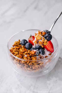 Mermer bir yüzey üzerinde yoğurt, çilek ve yaban mersinli lezzetli bir kase granola.