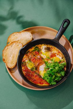 Geleneksel shakshuka ile domates soslu haşlanmış yumurta dökme demir tavada servis edilir, yanında da dilimler.