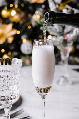 Kutlama şampanyası zarif bir flüt bardağına dökülüyor ve arka planda bayram ışıkları var.