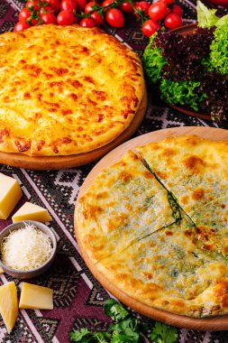 İki peynirli pizza ya da tahta tahtada khachapuri, dekoratif masa örtüsünün taze malzemelerinin yanında.