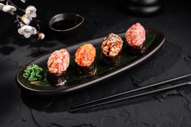 Suşi rulo çeşitleri geleneksel aksesuarlarla birlikte parlak siyah bir levhada servis edilir.