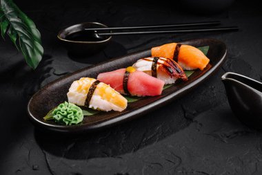 Soya soslu ve çubuklu siyah bir tabakta servis edilen nefis nigiri suşi seçimi.