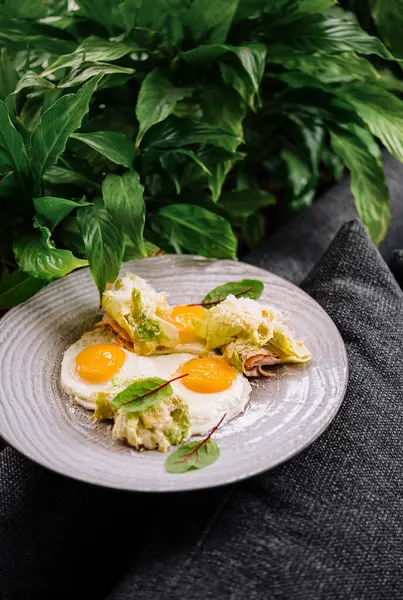 Seramik tabakta yeşil otlarla klasik Benedict yumurtalarının sanatsal sunumu