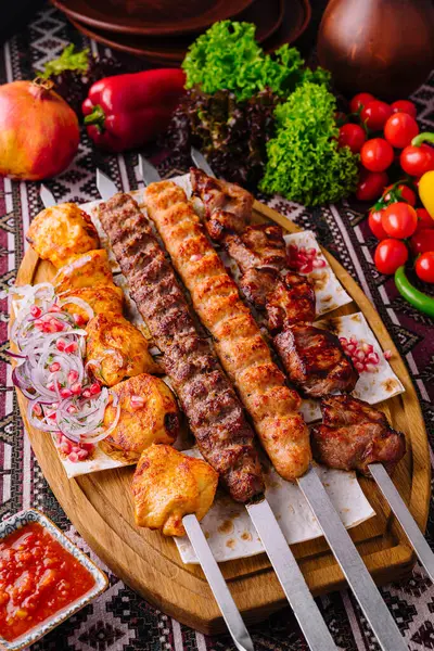 Lezzetli geleneksel barbekü şişi ızgara et, çeşitli sebzeler ve ahşap bir tahtada baharat sosu ile gurme yemek deneyimi için.