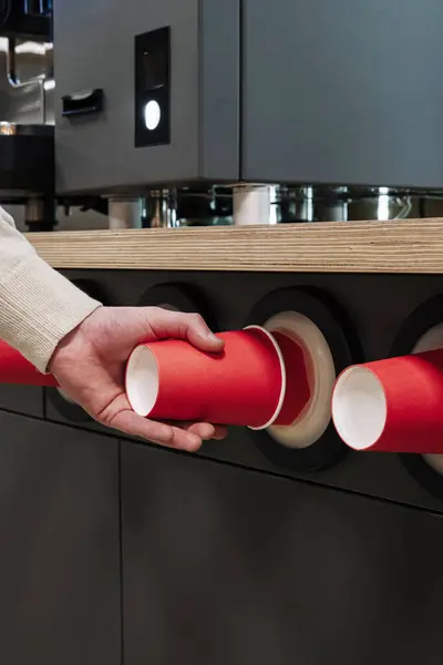stock image Close-up of a hand pulling a red paper cup from a modern cup dispenser in a cafeteria setting