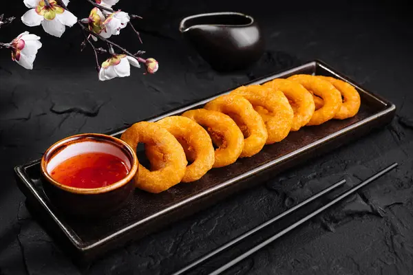 Golden-brown onion rings served on a slate tray with spicy dip and chopsticks, elegant food presentation