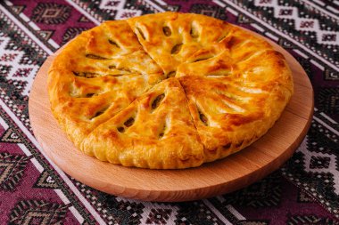 Yeni pişmiş Gürcü peynirli ekmek, Khachapuri, etnik desenli bir geçmişe sahip ahşap bir tahtada servis ediliyor.