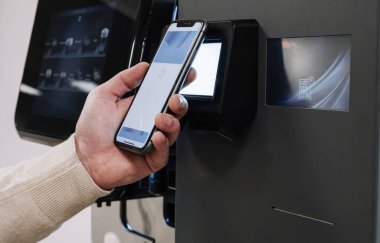 Elektronik bir ödeme istasyonunda, telefon kullanarak ulaşılamaz bir ödeme yapan kişi.