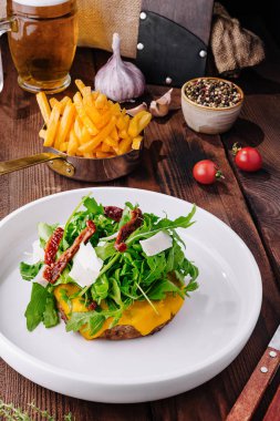 Lezzetli roka soslu çizburger, kenarları kırsal bir masada kurutulmuş domates.