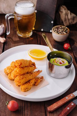 Keskin soslu kızarmış karides, taze garnitür ve ahşap masada bir bardak bira.