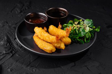 Taze salatayla servis edilen gurme karides ve iki soslu siyah tabak.