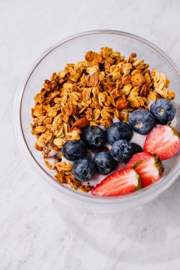 Gevrek granola, kremalı yoğurt ve olgun böğürtlenli besleyici kahvaltı kasesi.