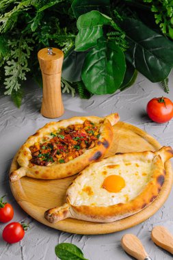 Adjarian ve Imeretian Khachapuri, taze domateslerle servis edilir ve bitkilerle çevrilidir.