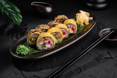 Şık bir seramik tabakta susam tohumlarıyla süslenmiş taze suşi ruloları, yemek çubukları ve soya sosuyla birlikte.